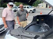Two men stand in front of an electric F 150 open hood bed.