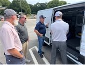 Four men stand in front of the side entrance of an electric transit vehicle