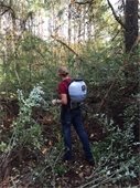 Back of young woman in woods wearing pesticide backpack sprayer.