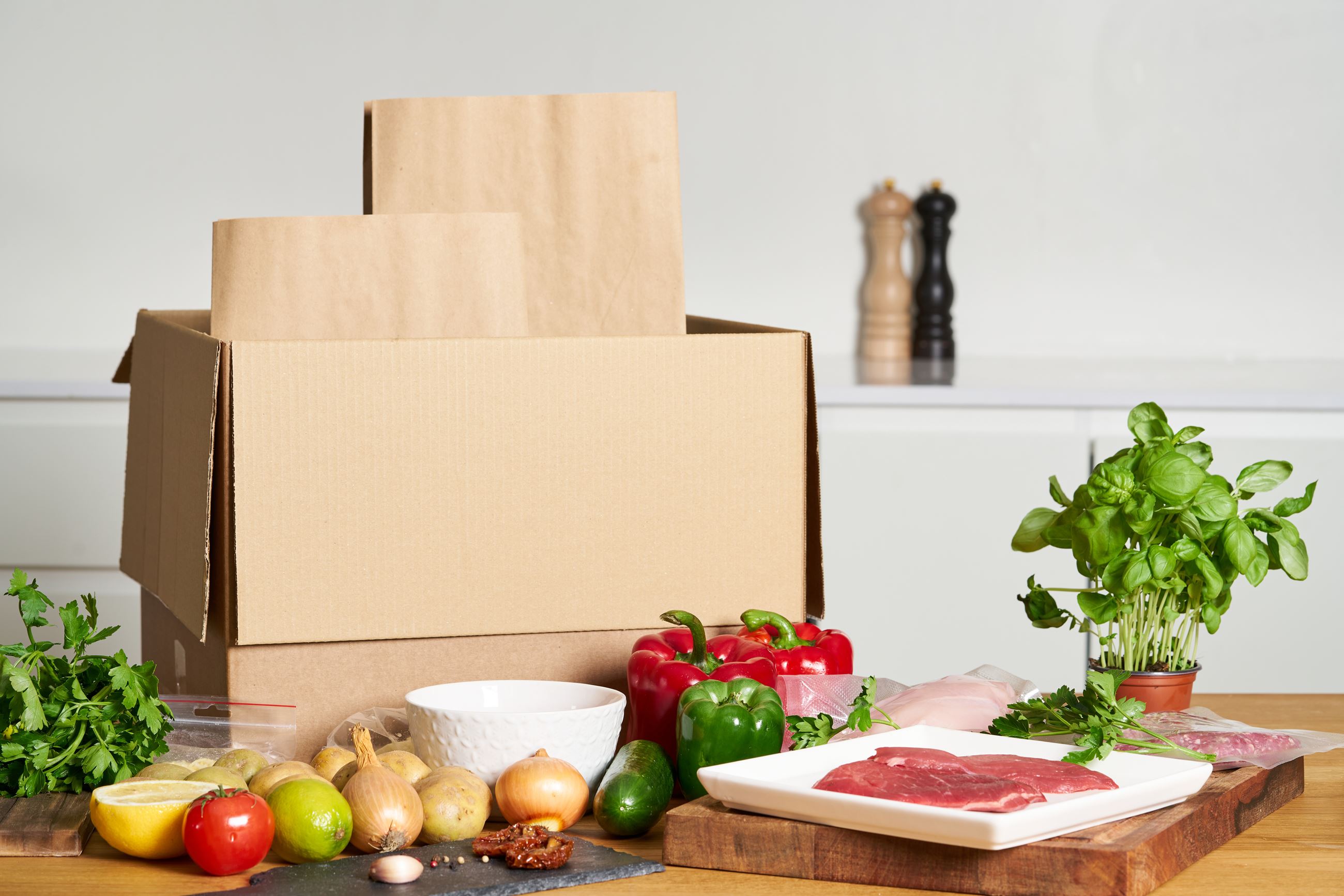 A cardboard box with tomatoes, meat, onions, and other raw foods on the counter to use for a meal